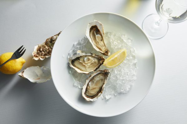 Oysters with lemon on plates Opened oysters with piece of lemon in the white plate, glass of wine and cutlery. View from above